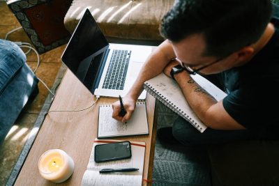 man working from home in living room with laptop and notepad